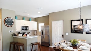 A modern kitchen with white cabinets, a stainless steel refrigerator, and a dining area with wooden furniture and a chandelier. - Fd57055 - Lucaya Village - 4 Bed 3 Baths Townhouse (Kissimmee)