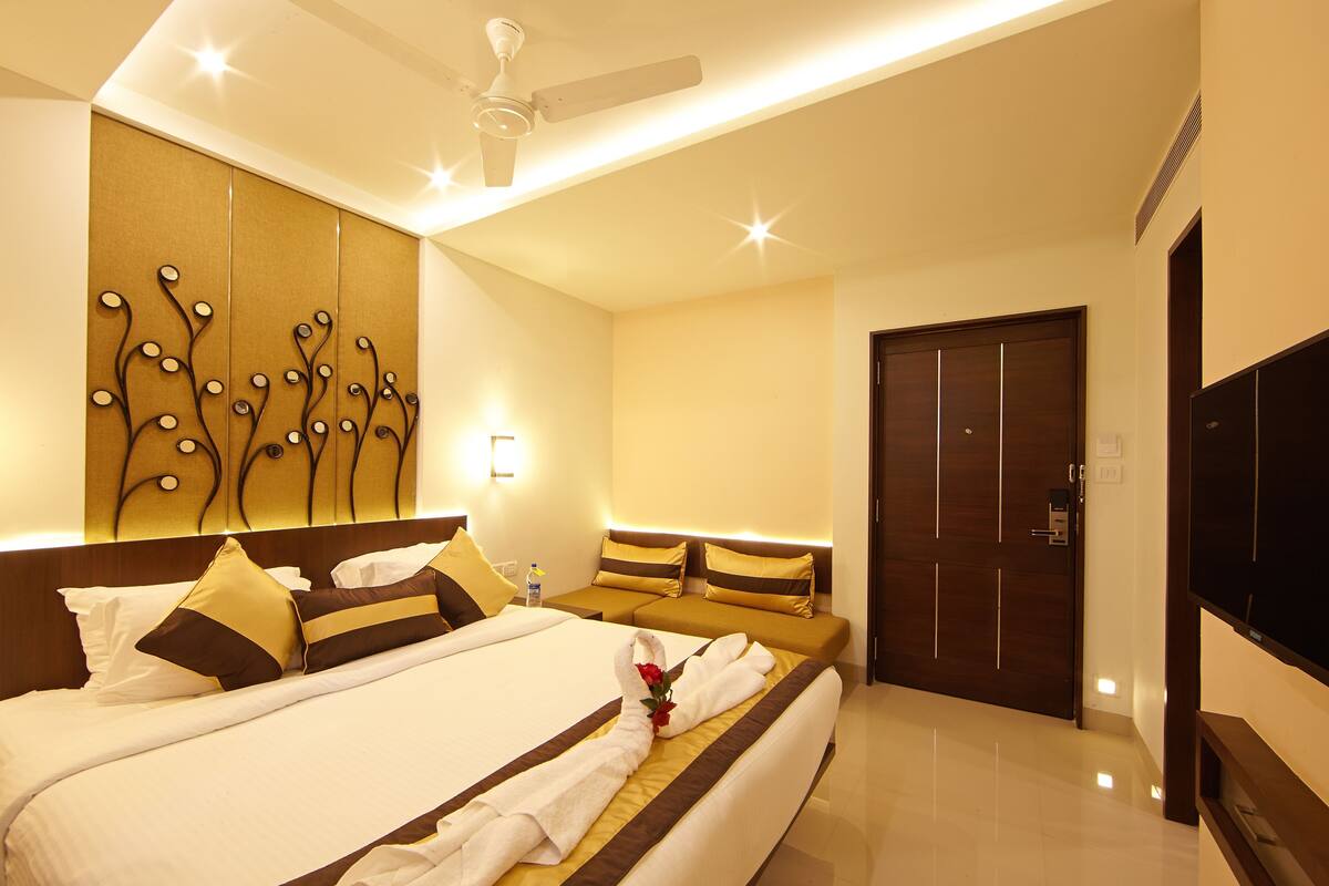 A hotel room with a bed, bedside table, wall art, ceiling fan, and a TV.