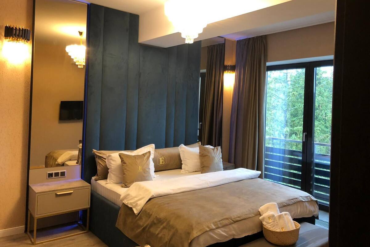 Habitación de hotel moderna con una cama grande, una mesita de noche, un espejo y vistas al exterior.