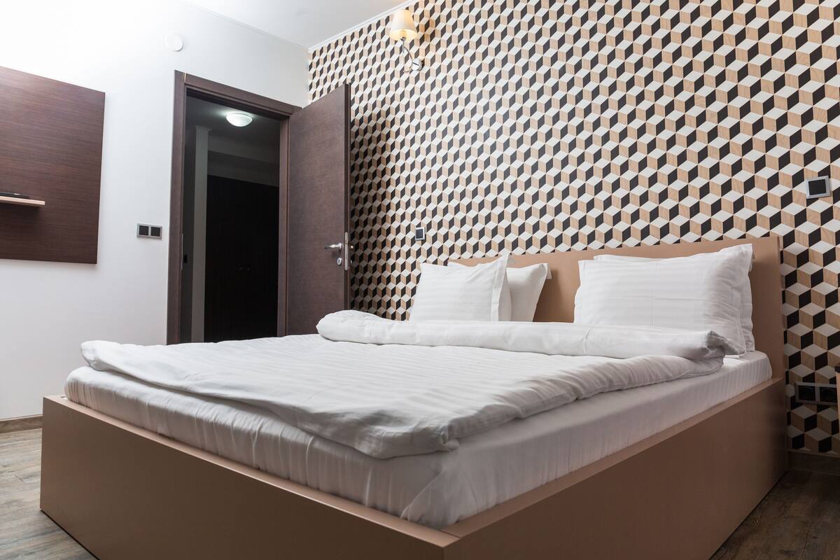 Un dormitorio moderno con una pared de estampado geométrico, un cabecero de madera y una estructura de cama empotrada.