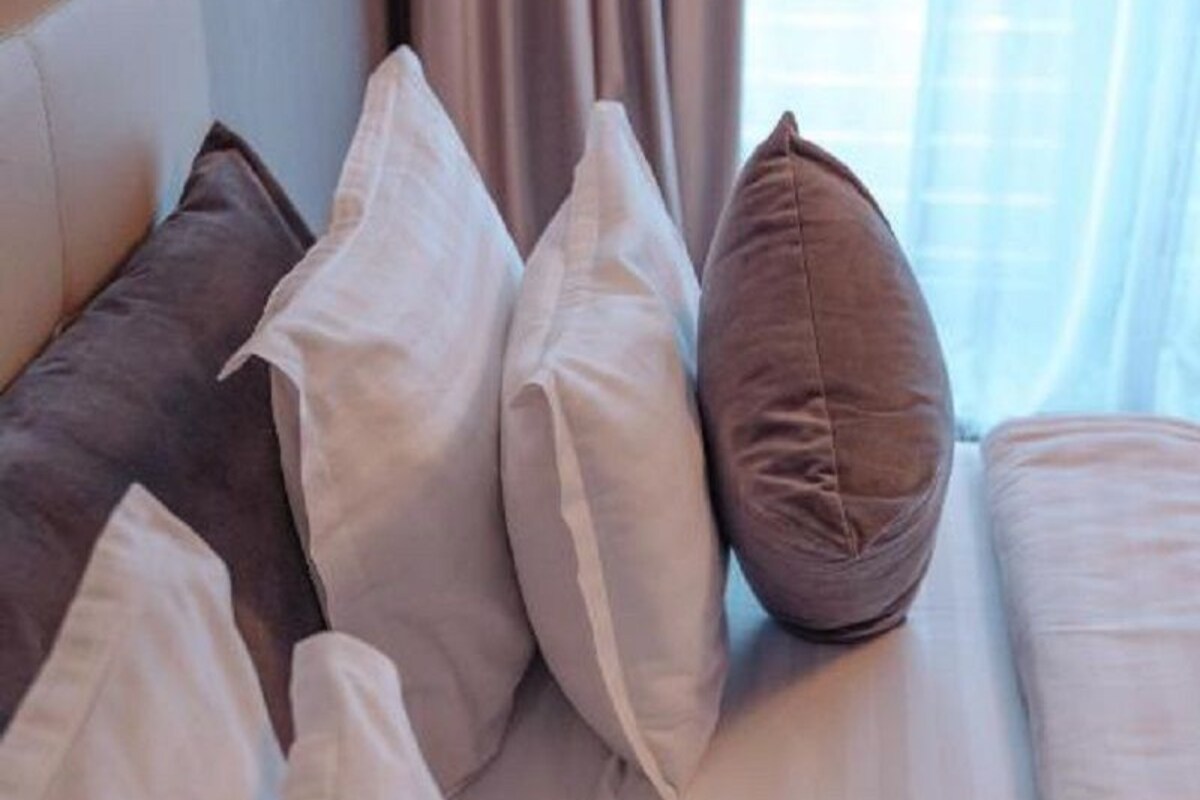 A hotel room with a bed, pillows, and curtains.