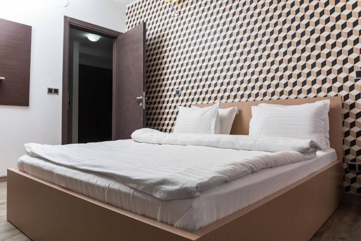 Un dormitorio moderno con una cama, cabecera de madera y pared con estampado geométrico.
