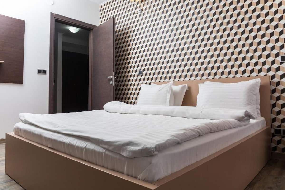 Un dormitorio moderno con una cama, cabecera de madera y pared con estampado geométrico.
