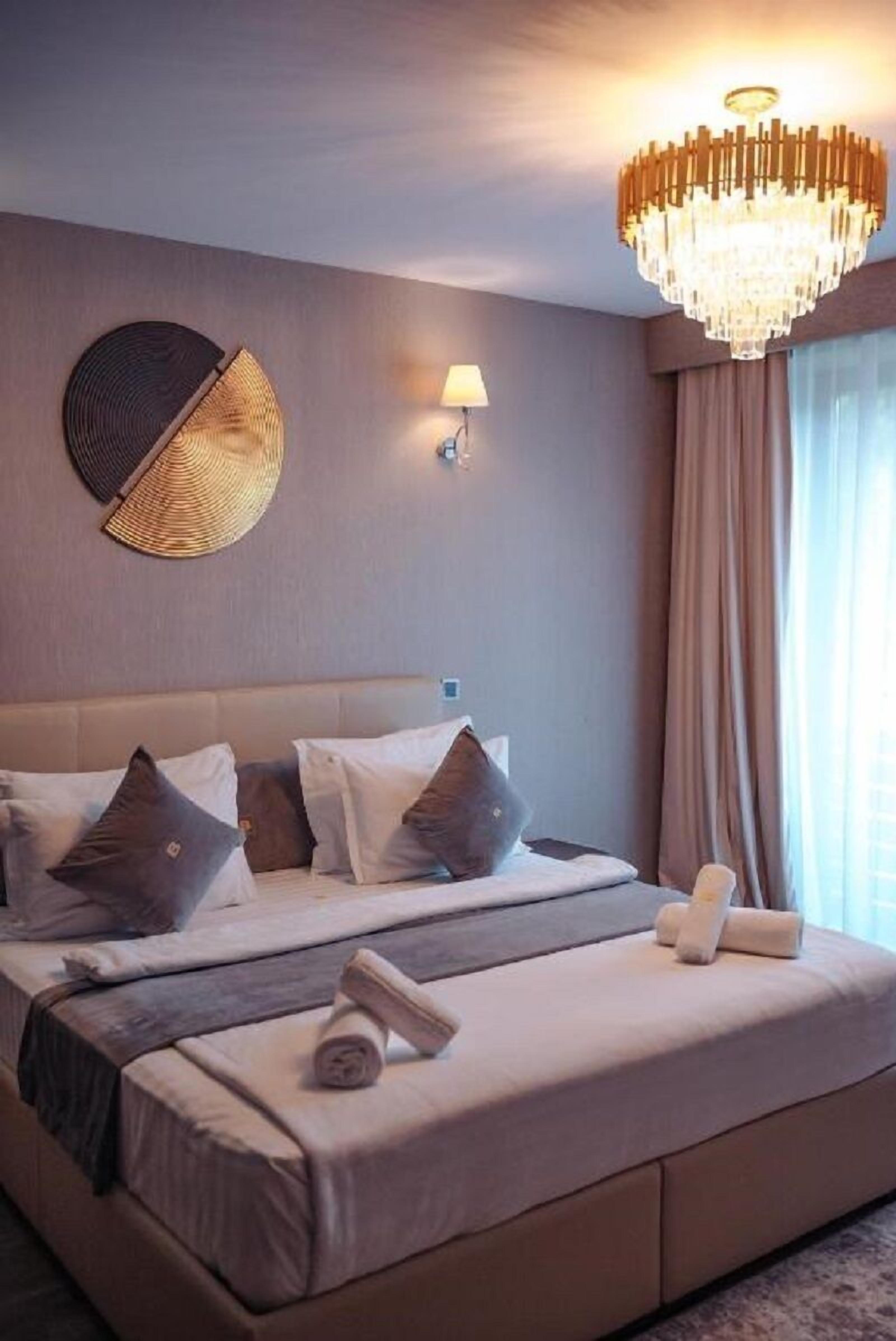 Una habitación de hotel con una cama grande, un candelabro, una lámpara de pared y un ventanal con cortinas.