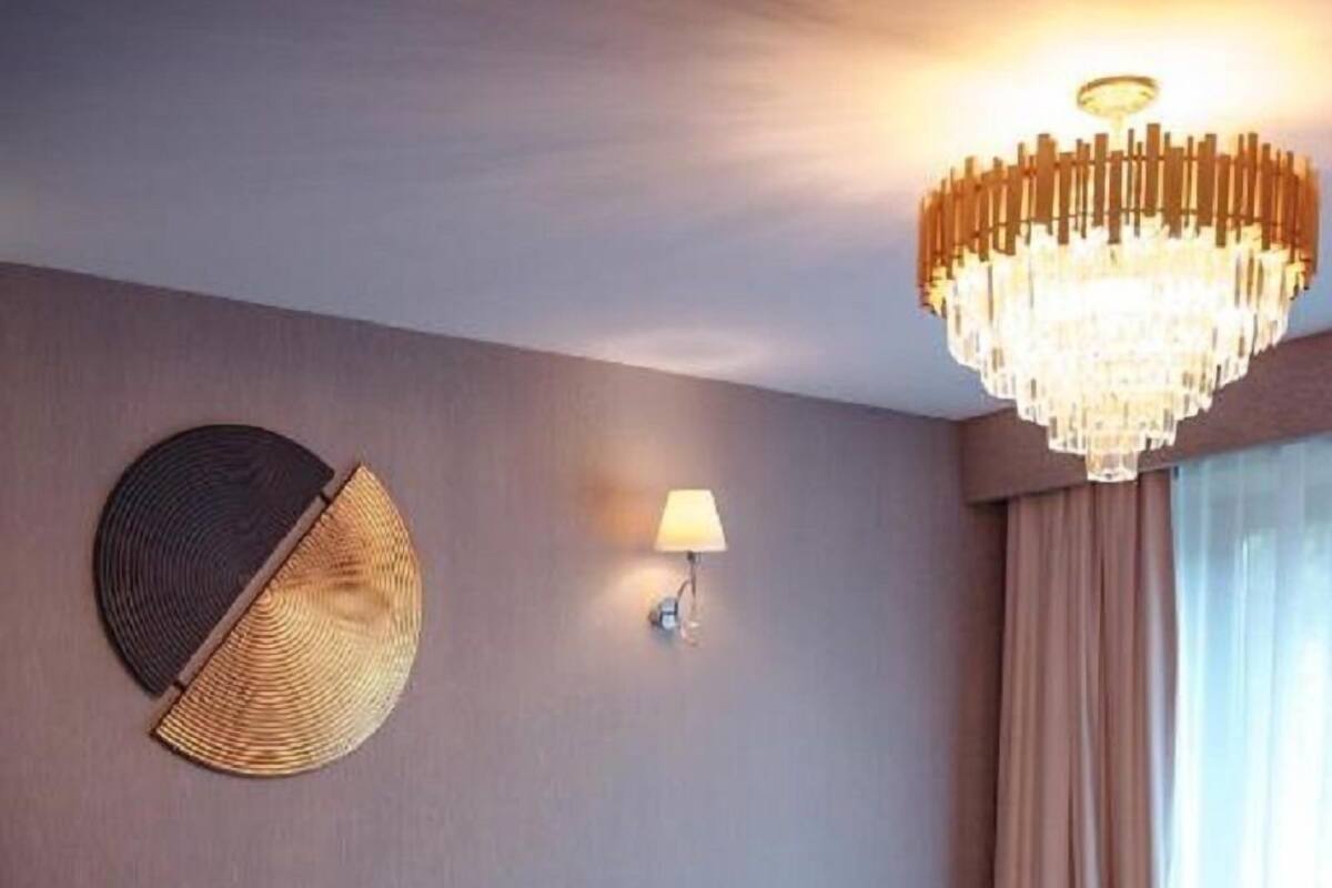 Una habitación de hotel con una cama grande, un adorno circular en la pared, una araña y una ventana con cortinas.