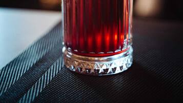 Un vaso alto con una bebida roja, adornado con una cuña de lima, frambuesa y una hoja.