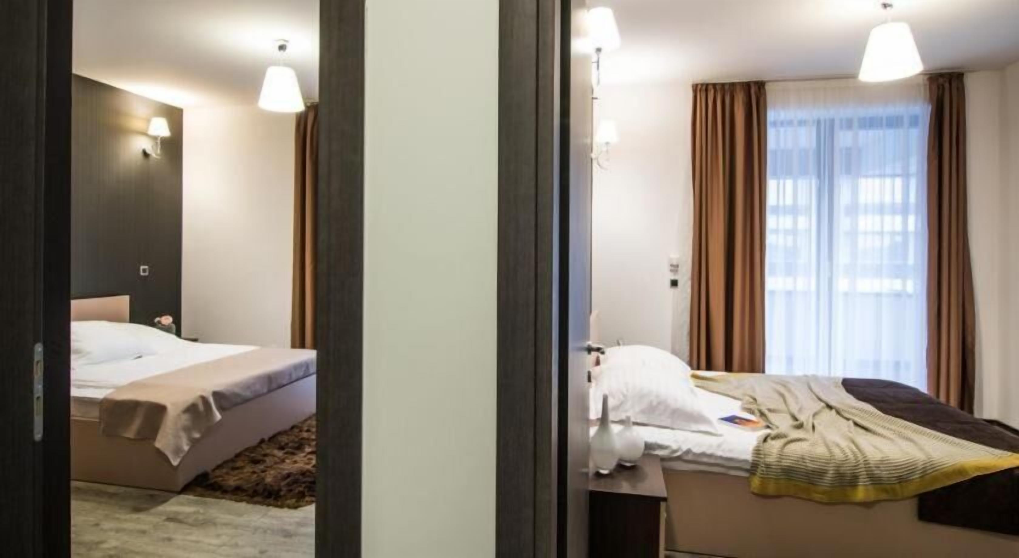 Una habitación de hotel con cama, mesita de noche, lámpara y ventana con cortinas.