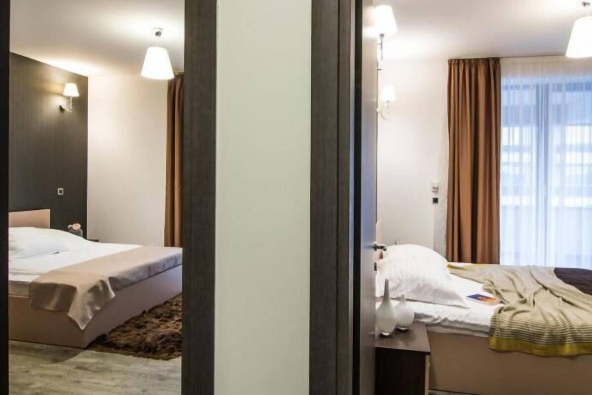 Una habitación de hotel con cama, mesita de noche, lámpara y ventana con cortinas.