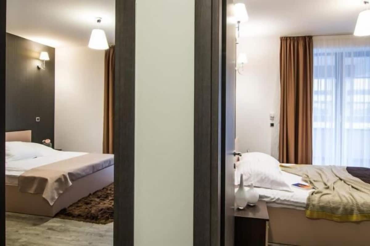 Una habitación de hotel con cama, mesita de noche, lámpara y ventana con cortinas.