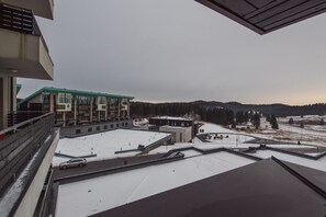 A building with multiple floors, a parking area, and a snowy landscape with trees and hills in the background. - Silver Mountain Resort & SPA (Brasov)