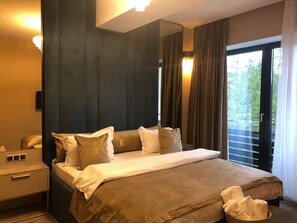A hotel room with a large bed, a bedside table, a mirror, and a view of the outdoors through a window. - Silver Mountain Resort & SPA (Brasov)