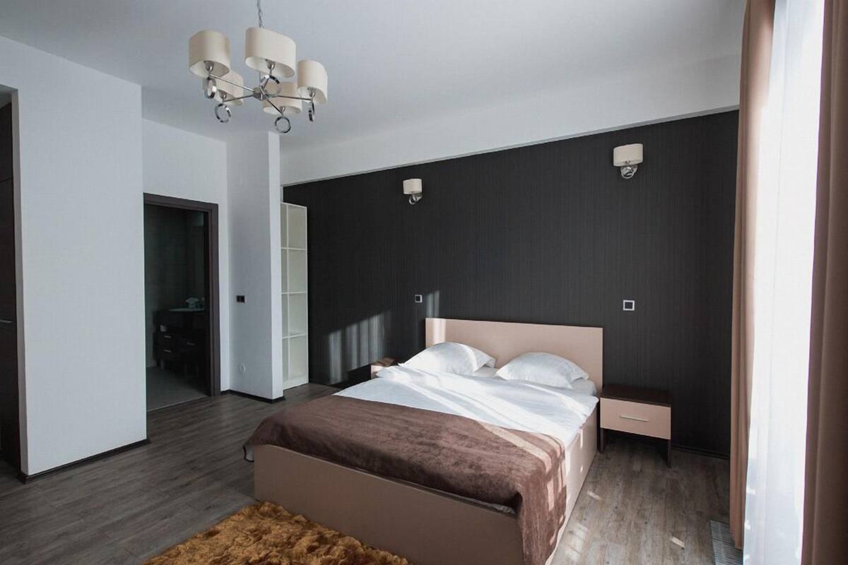 Un dormitorio moderno con una cama grande, mesitas de noche, una araña y un armario.