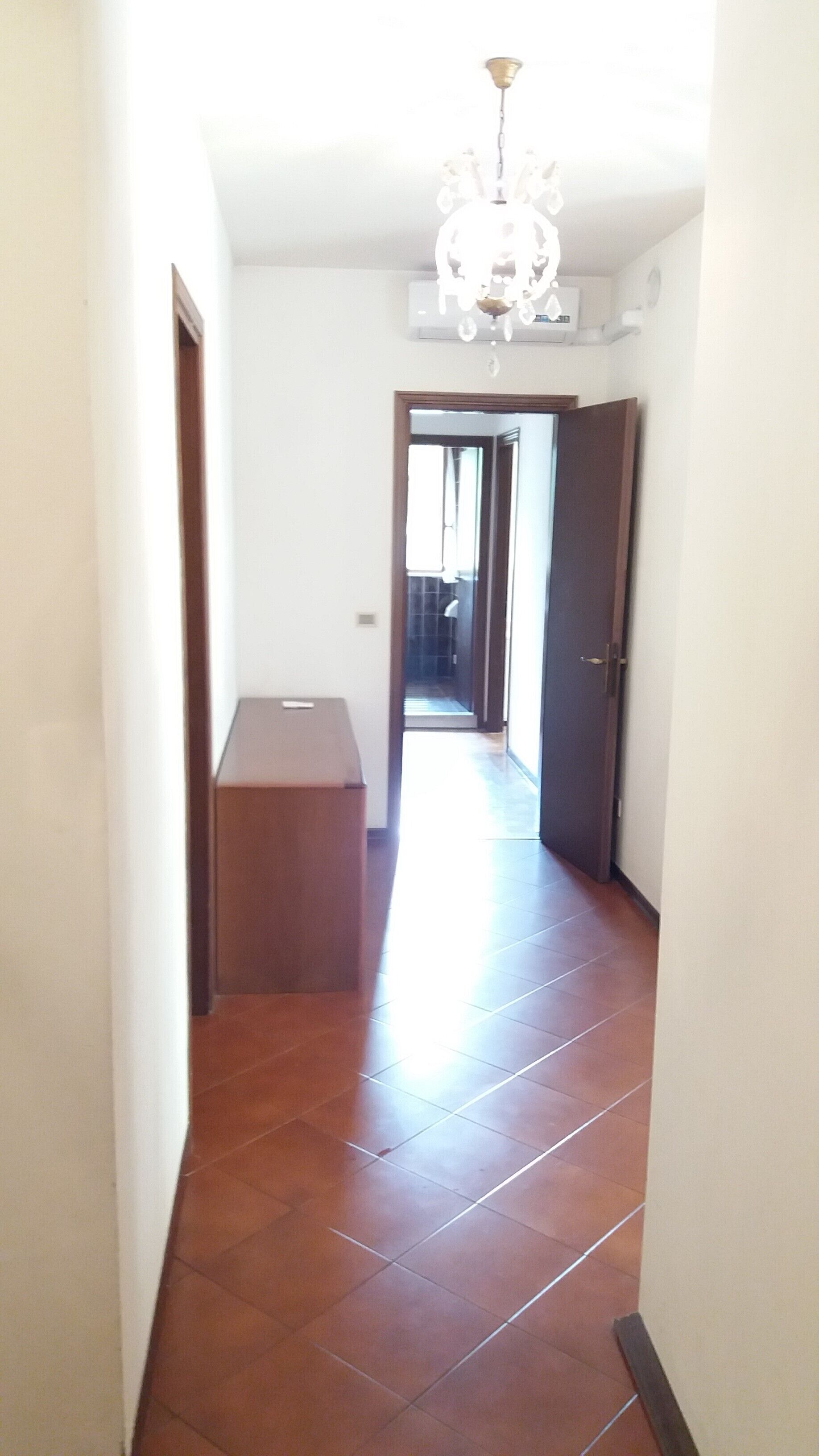 A hallway with a chandelier, a wooden bench, and a door leading to another room.
