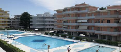 A swimming pool area with multiple pools, surrounded by apartment buildings.
