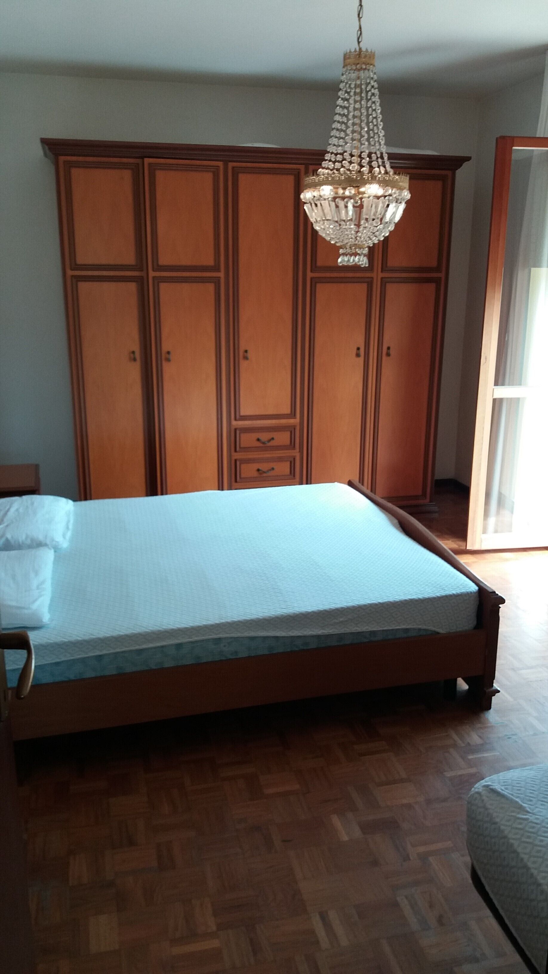 A bedroom with a wooden bed, a large wardrobe, and a chandelier.