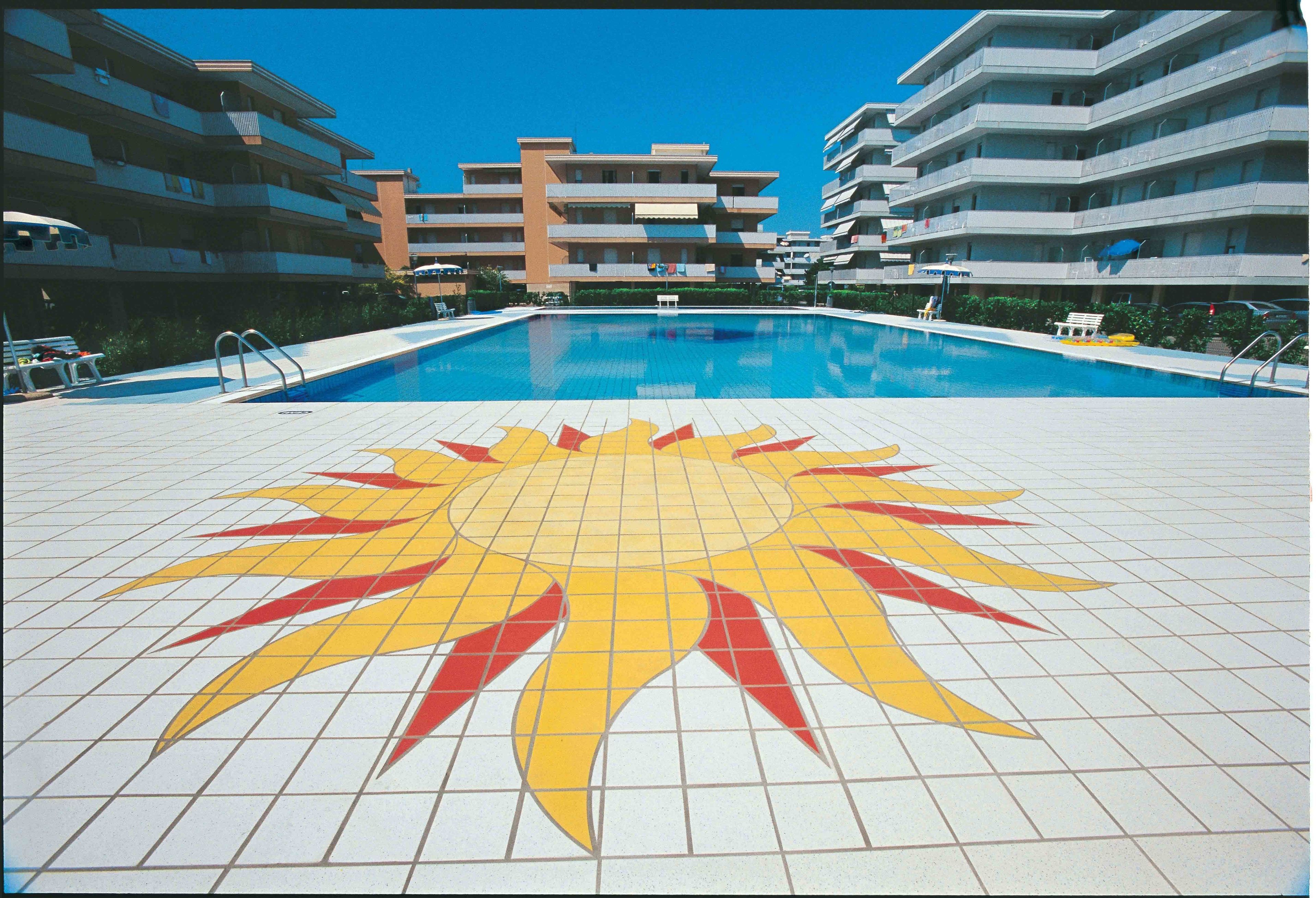 Ein Schwimmbecken mit Sonnendesign auf dem Boden, umgeben von mehrstöckigen Gebäuden.