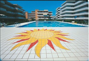 Une piscine dont le fond est décoré d’un motif solaire, entourée d’immeubles à plusieurs étages.