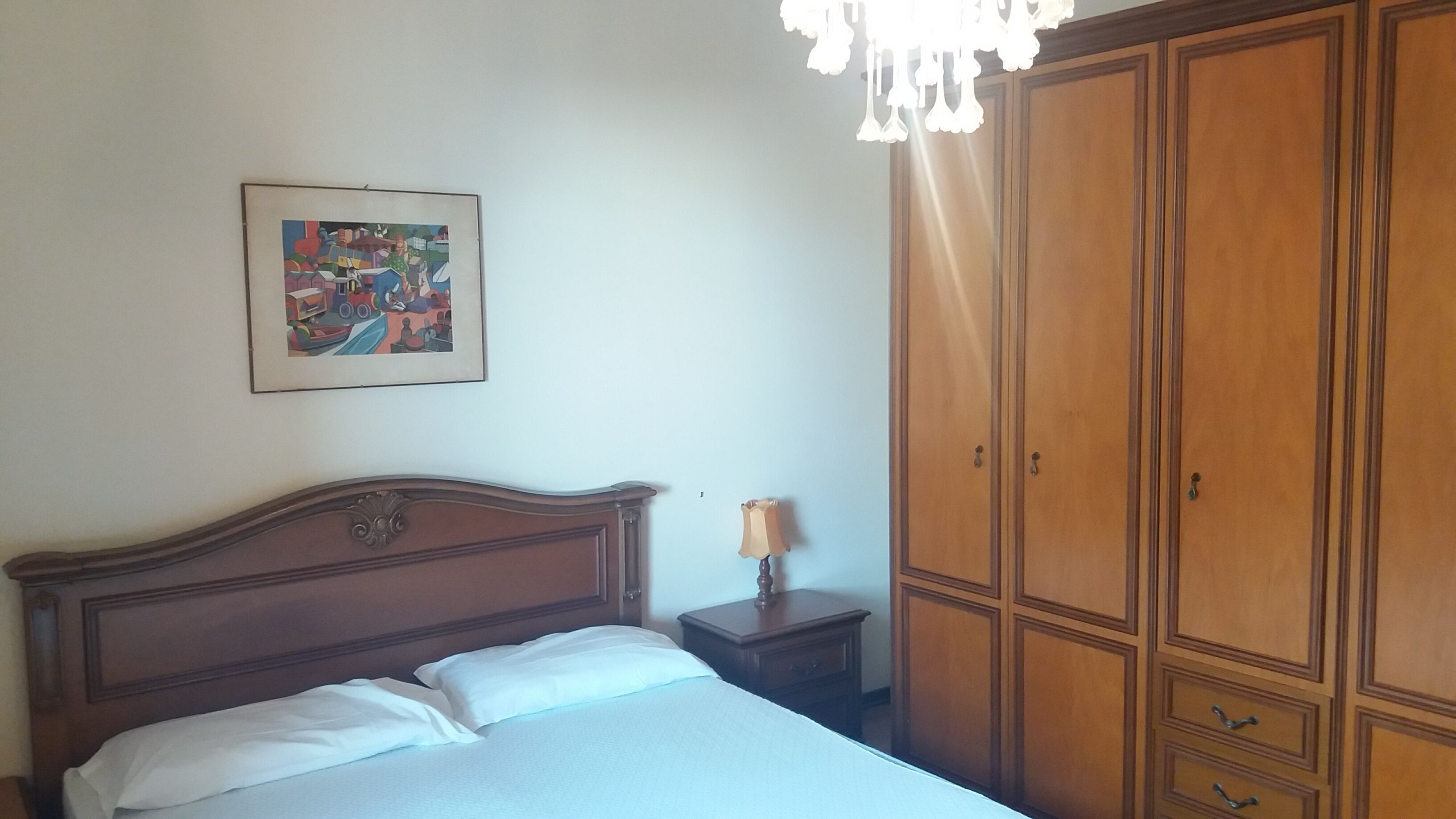 Un dormitorio con cama de madera, mesita de noche, lámpara, armario y un cuadro en la pared.