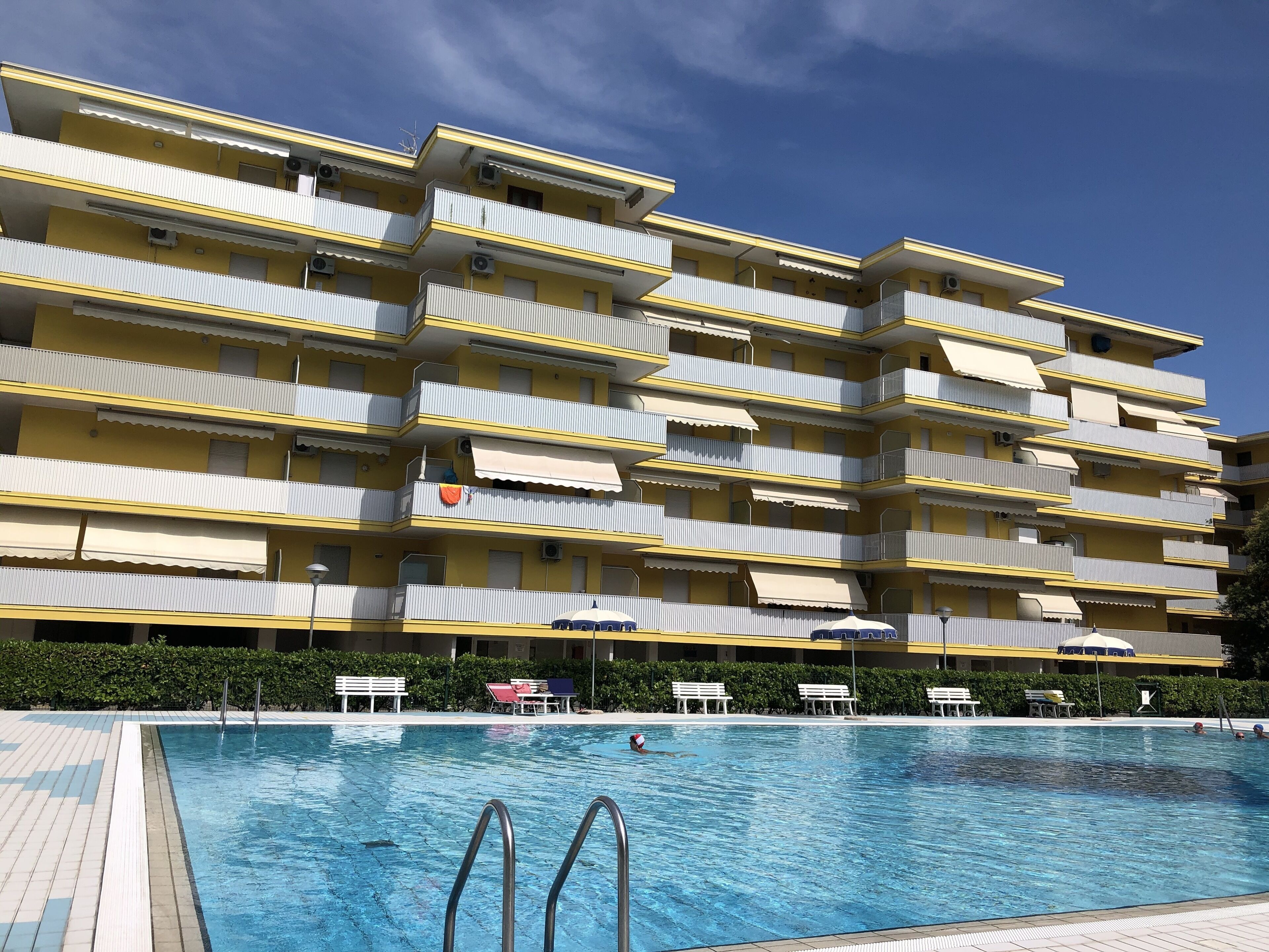 A multi-story yellow building with balconies, a swimming pool, and outdoor seating.