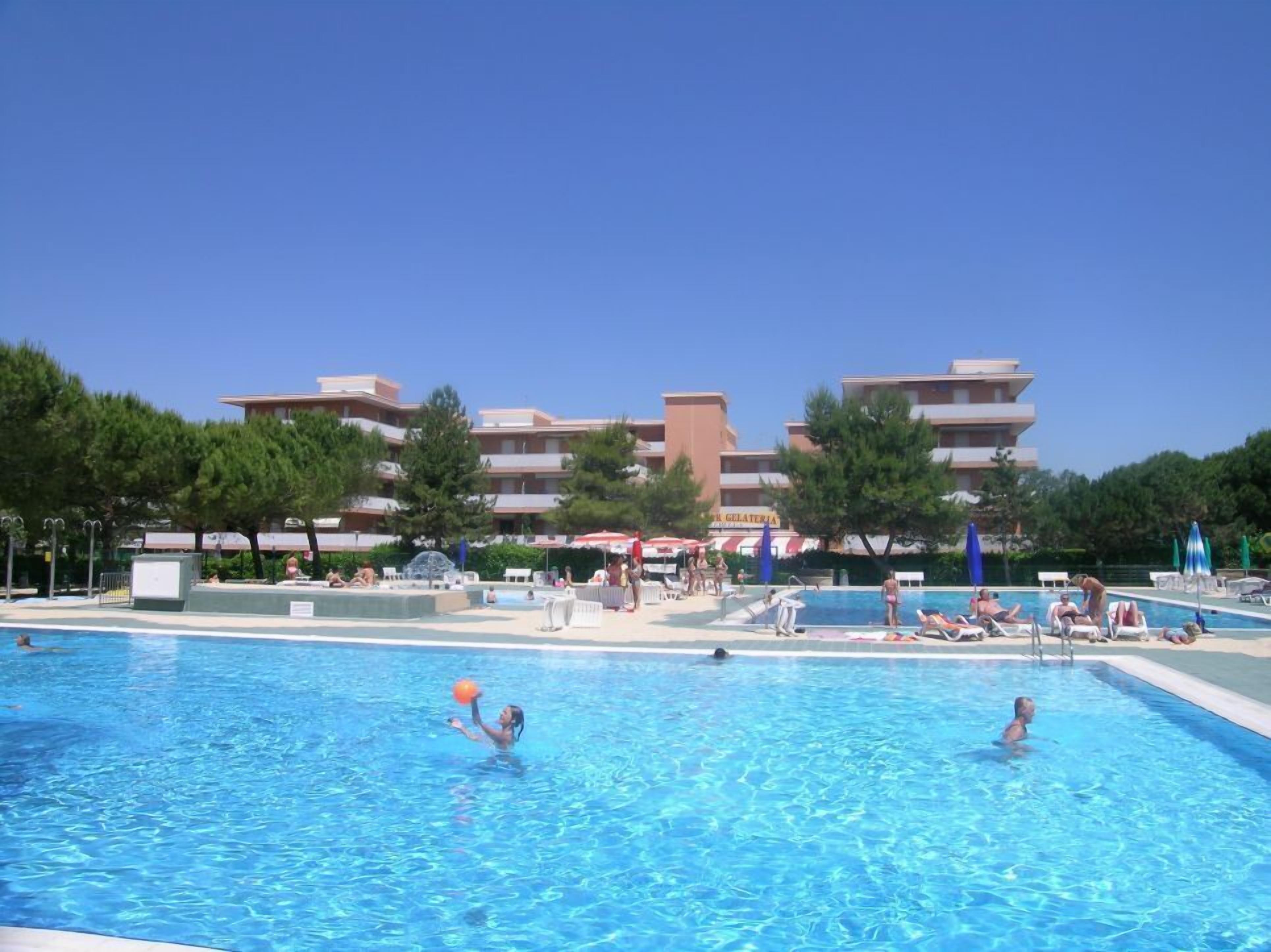 A swimming pool area with multiple pools, lounge chairs, and umbrellas.
