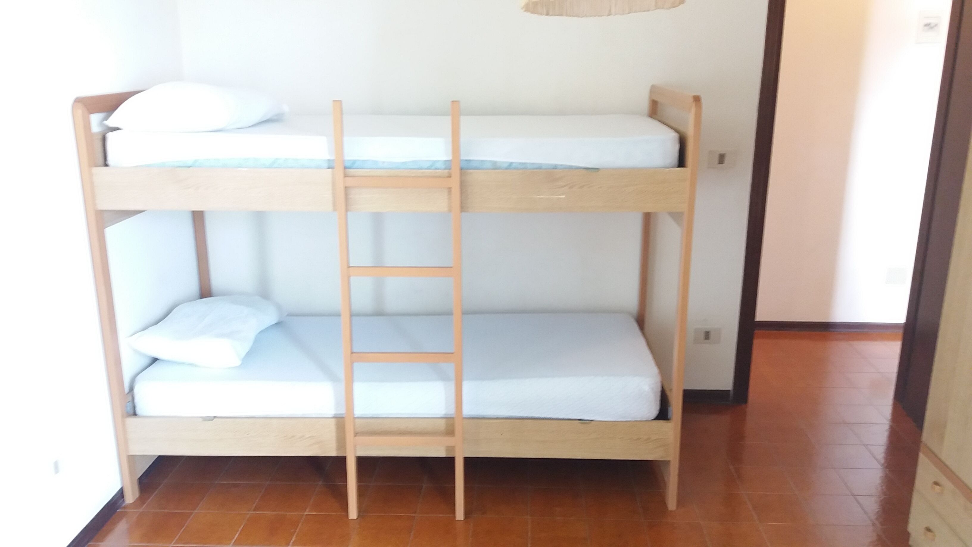 A bunk bed with a ladder, white bedding, and a tiled floor.