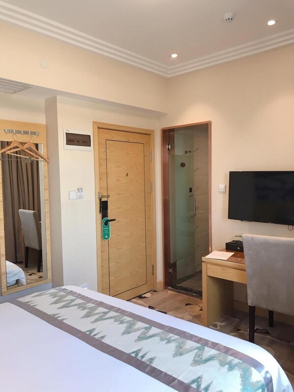 Una habitación de hotel con cama, escritorio, televisor, espejo y puerta.