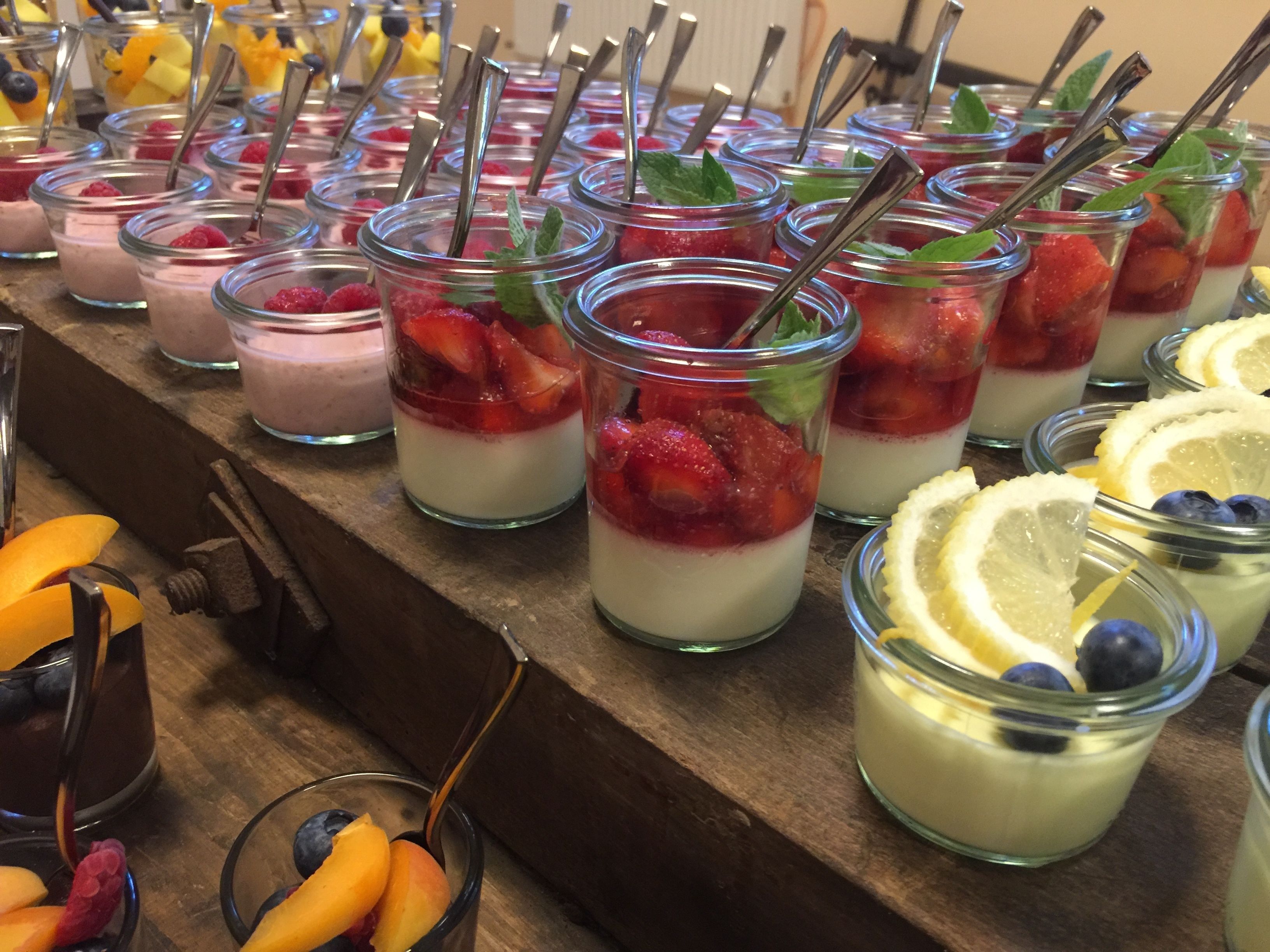 A variety of fruit parfaits in glass jars with metal straws, arranged on a wooden surface.