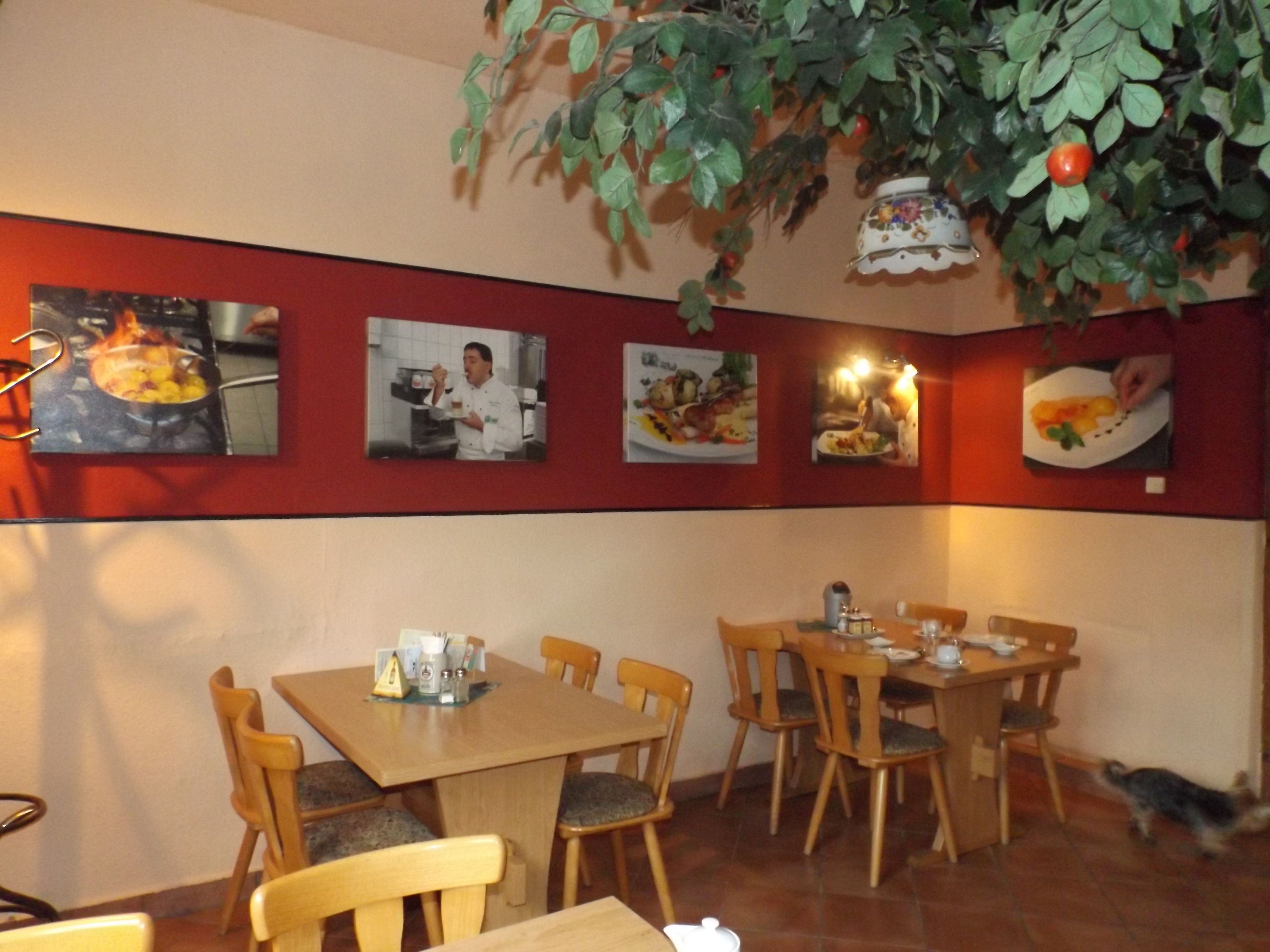 Un interior de restaurante con mesas y sillas de madera, una planta colgante y cuadros en la pared.