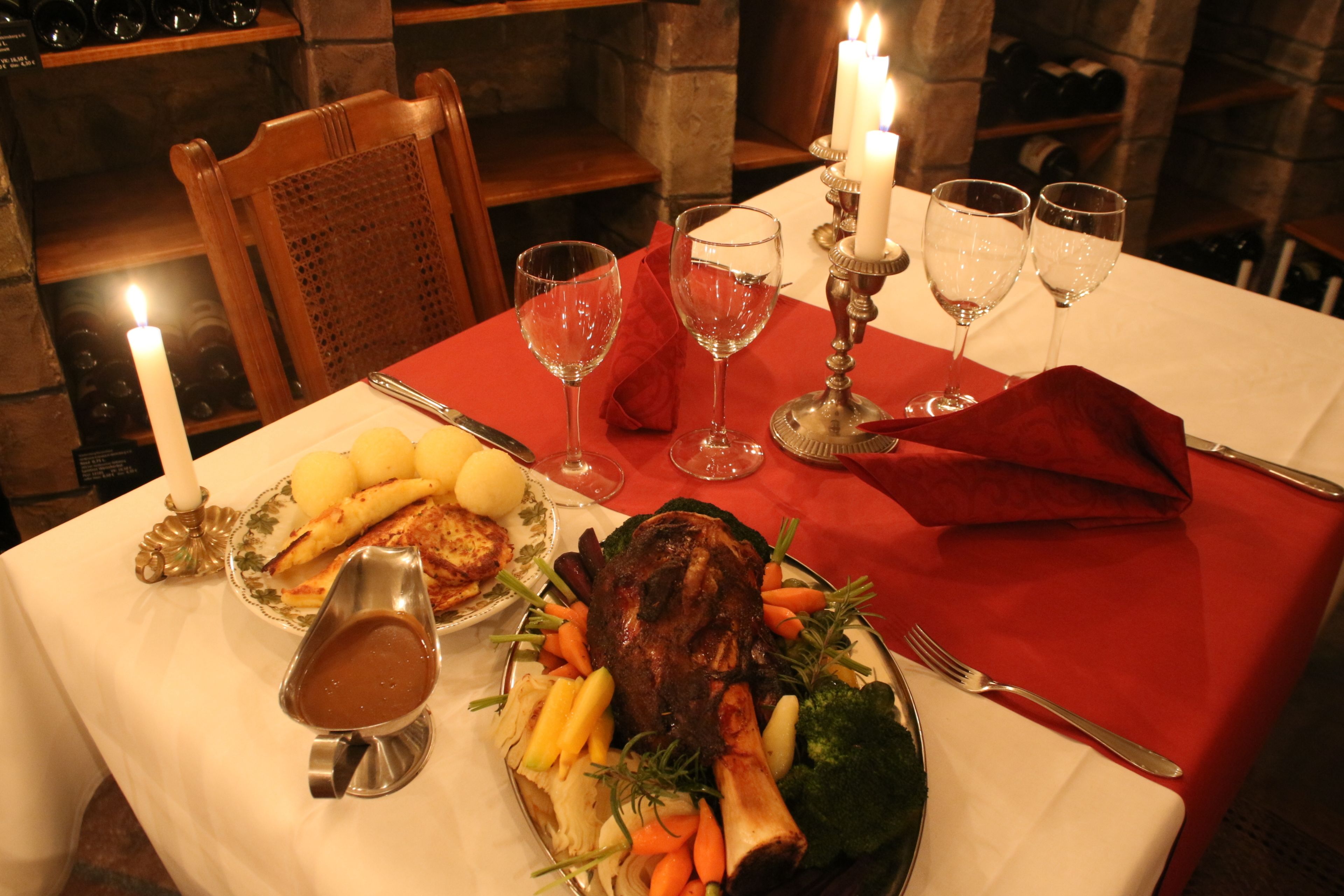 Una mesa de comedor con mantel rojo, un plato fuerte de carne asada y varios acompañamientos.