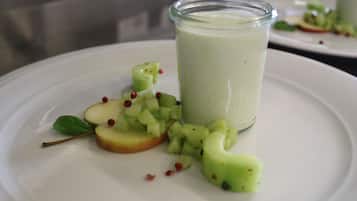 A white plate with a glass of green smoothie, apple slices, and a mint leaf.