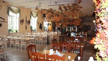 Un espace repas avec plusieurs tables et chaises, un grand arbre aux feuilles d’automne et un escalier en arrière-plan.