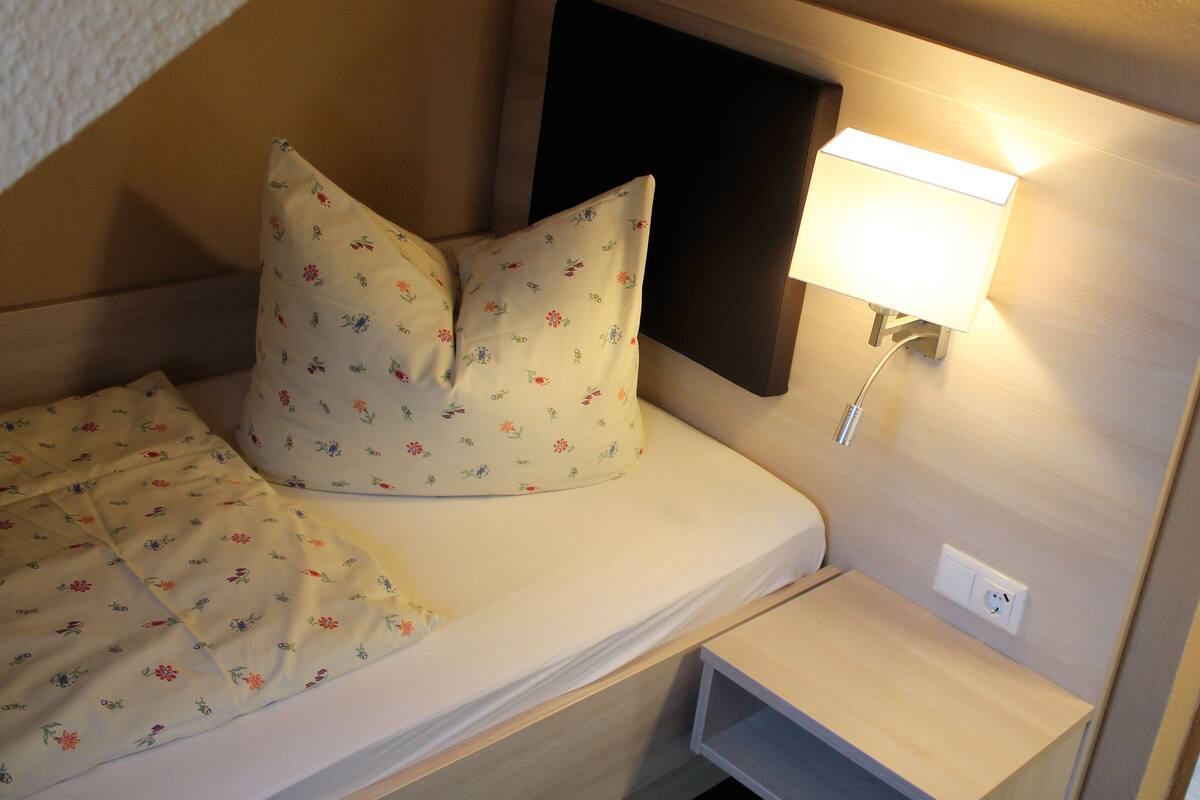 Una cama individual con ropa de cama floral, una mesita de noche y una lámpara de pared.