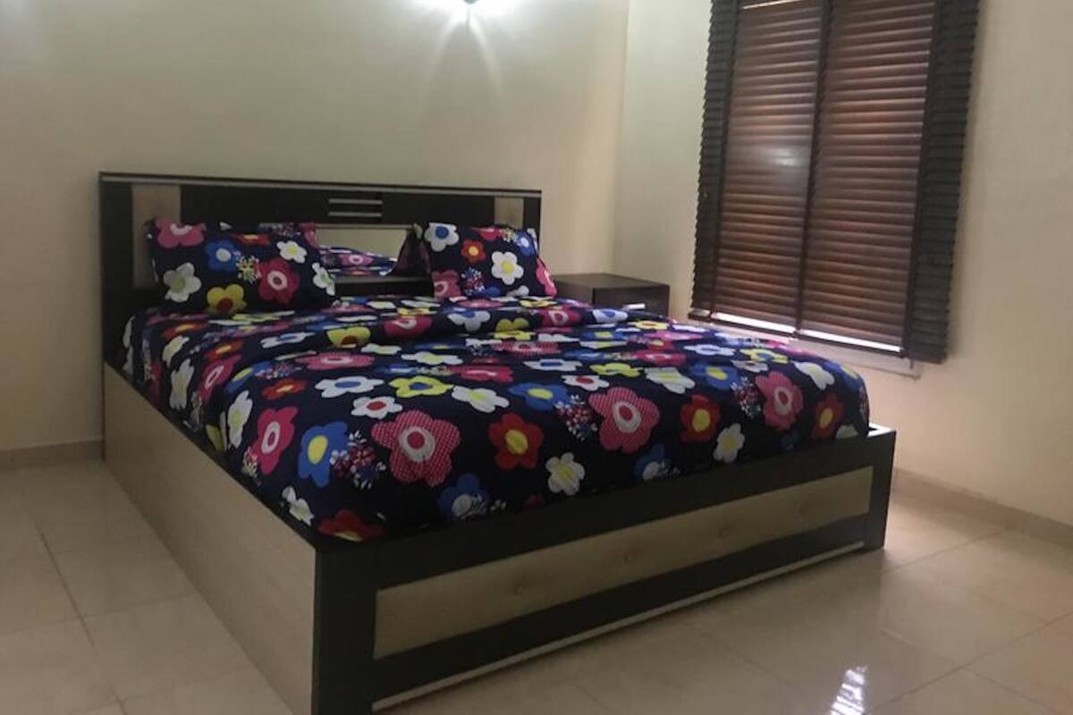 A bed with a floral bedspread in a room with a tiled floor and a window with blinds.