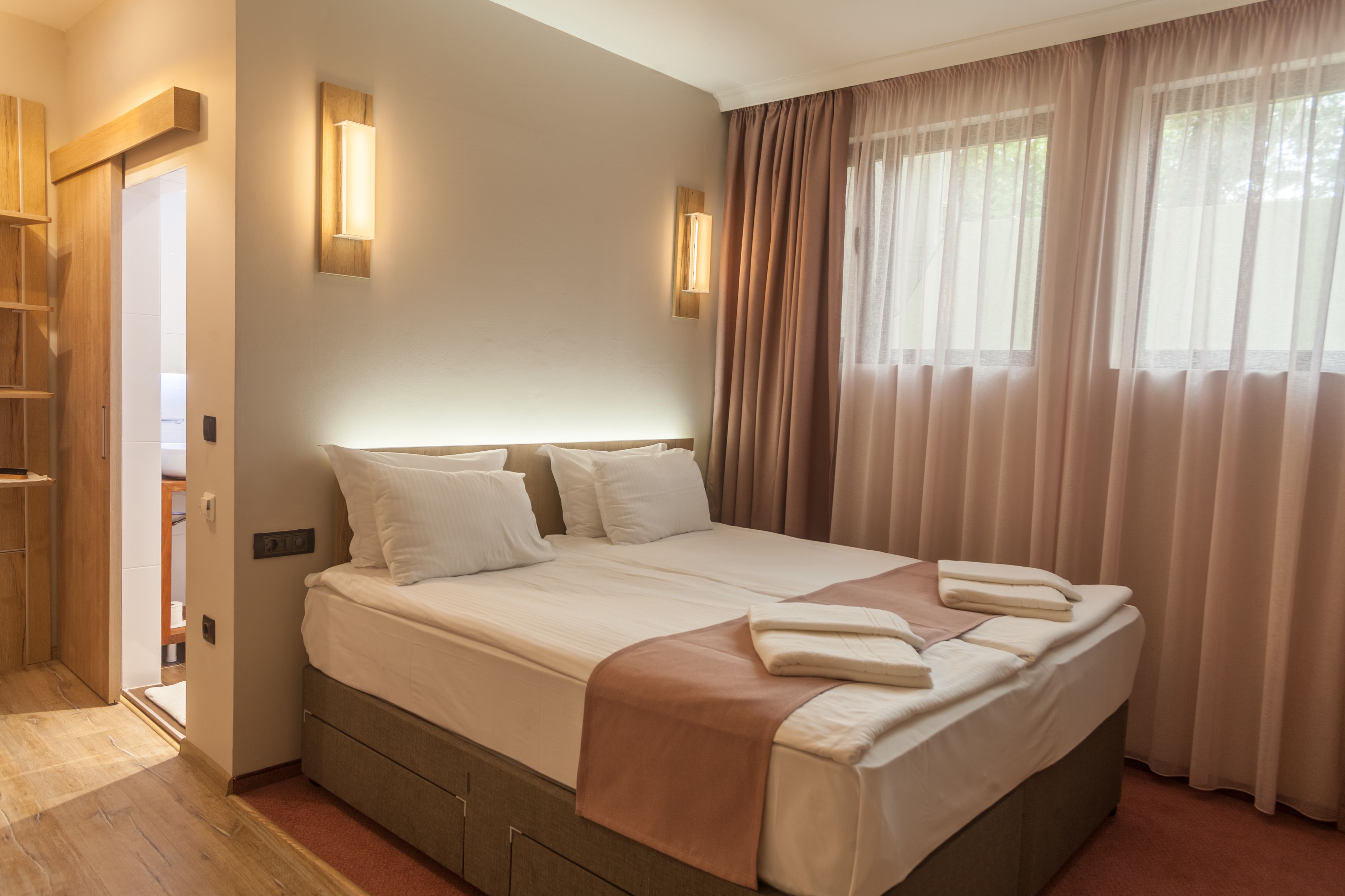 Una cama bien hecha con almohadas y una colcha, un armario de madera y una lámpara fijada a la pared.