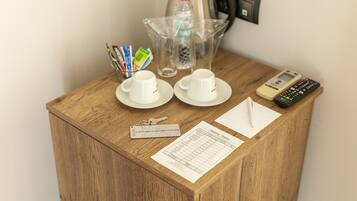 A wooden side table with a kettle, a water bottle, two cups, a remote control, a keychain, and a form on it.