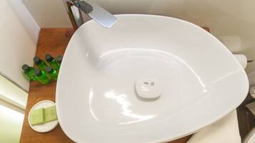 A white oval sink with a chrome faucet, a soap dish, and several green bottles on a wooden countertop.