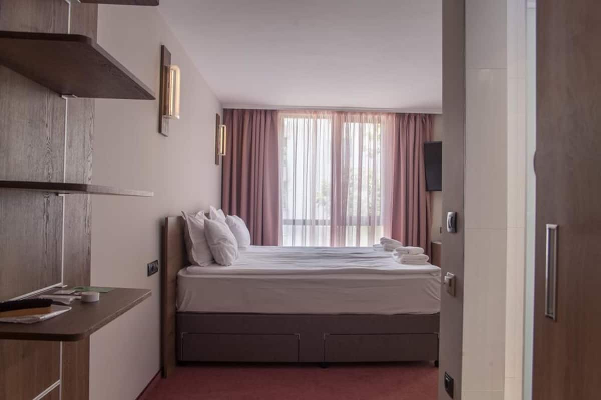 Quarto de hotel com cama, mesa de cabeceira e janela com cortinas.