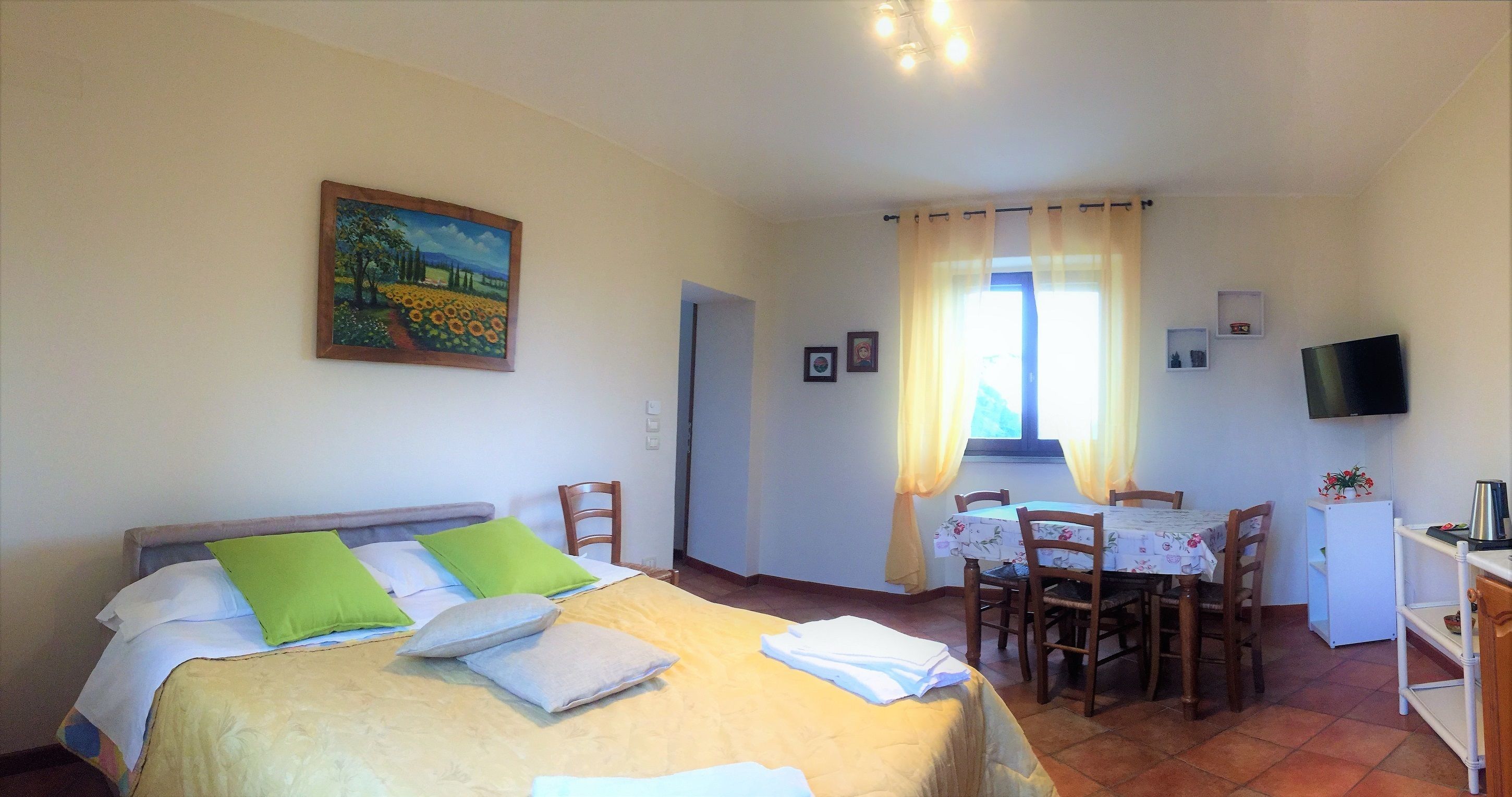 A room with a bed, a dining table with chairs, a television, and a window with curtains.