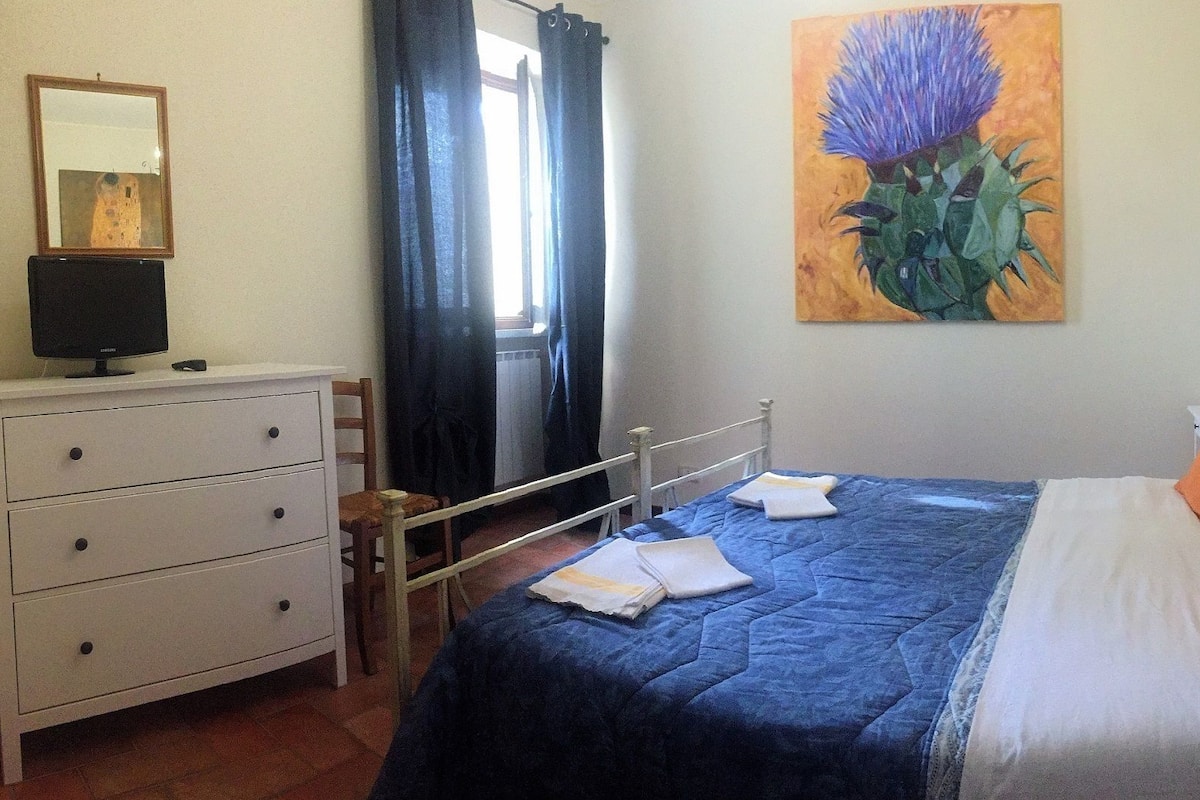 Un dormitorio con una cama, un aparador, una silla, un cuadro y una ventana con cortinas.