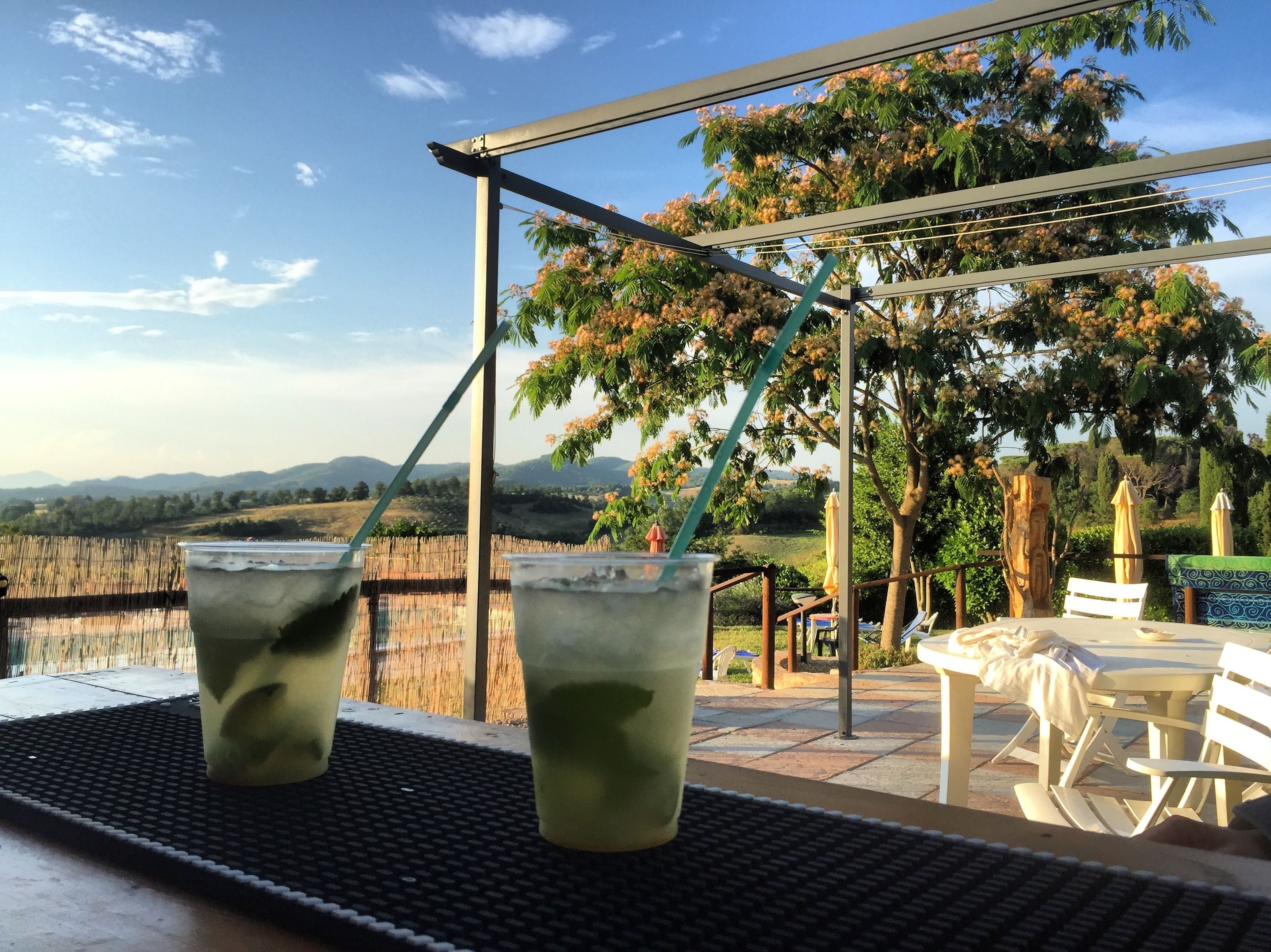 A terrace with two glasses of iced tea, a wooden fence, and a view of distant hills.