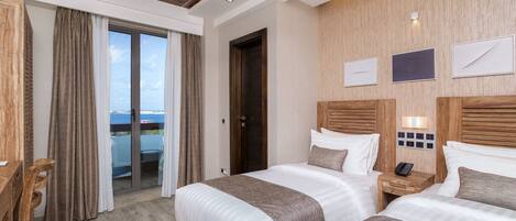 A hotel room with two beds, a wooden headboard, a small bedside table with a lamp, and a view of the outdoors through a sliding door.