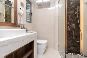 A modern bathroom with a marble sink, a toilet, and a glass-enclosed shower area.