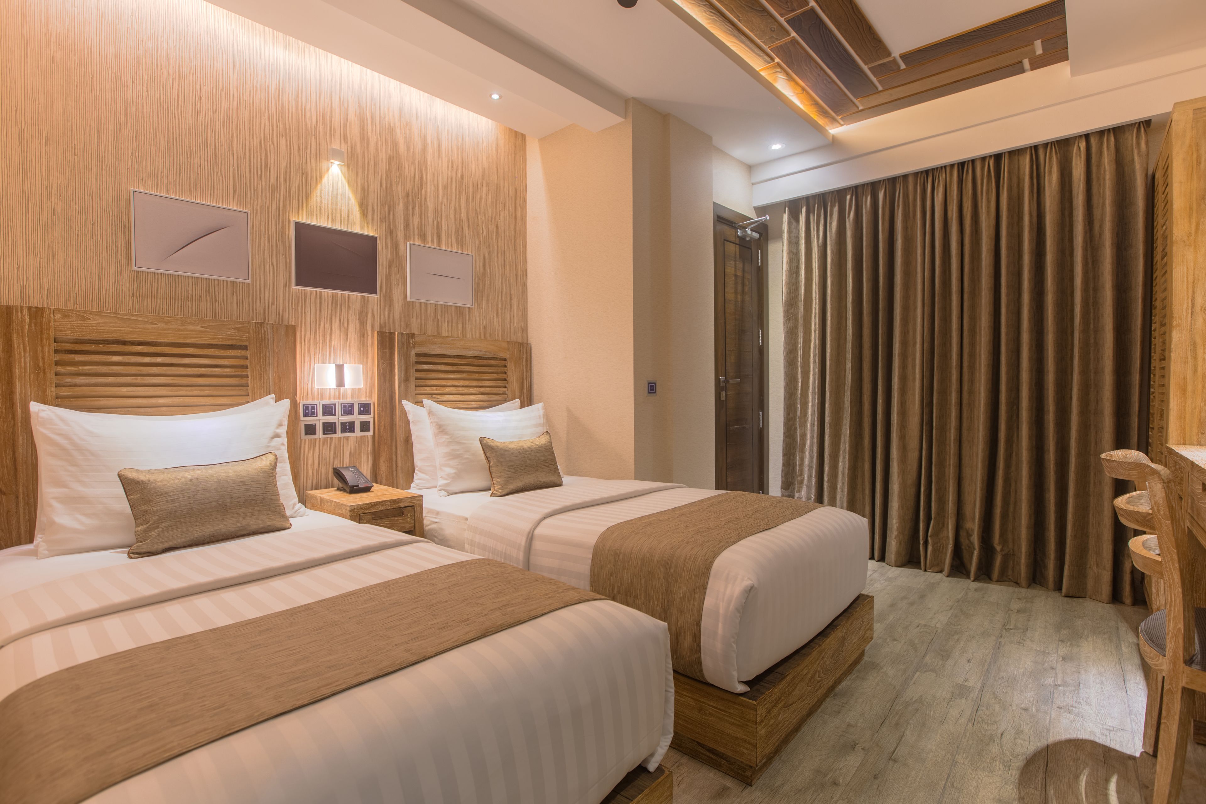 A hotel room with two beds, wooden headboards, a wooden desk, and a shower area.