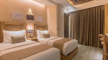 A hotel room with two beds, wooden headboards, a wooden desk, and a shower area.