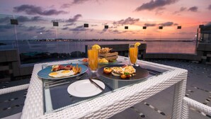 A table set with breakfast items and drinks, overlooking a scenic sunset view.