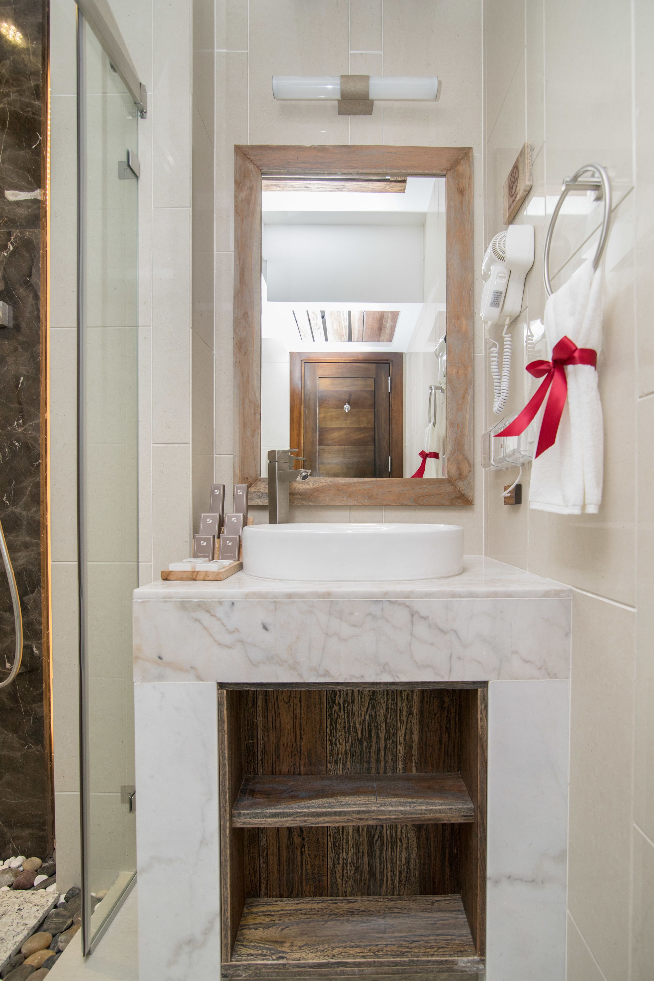 A bathroom with a marble sink, wooden vanity, and a glass shower enclosure.