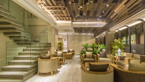 A modern hotel lobby with a glass staircase, plush seating, and a wooden ceiling.