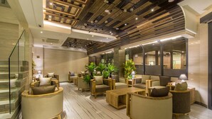 A modern lobby with a wooden ceiling, seating area with sofas and tables, and a staircase.