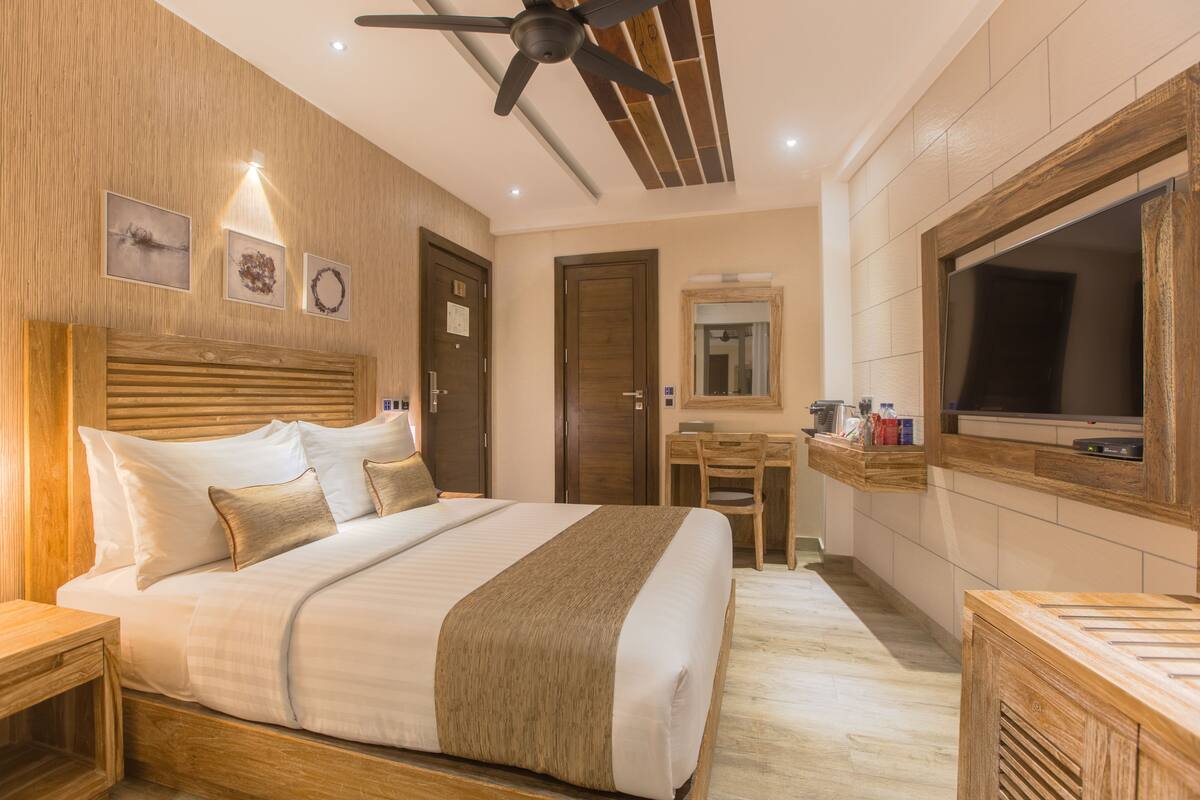A hotel room with a large bed, wooden headboard, ceiling fan, wooden desk, TV, and a mirror.