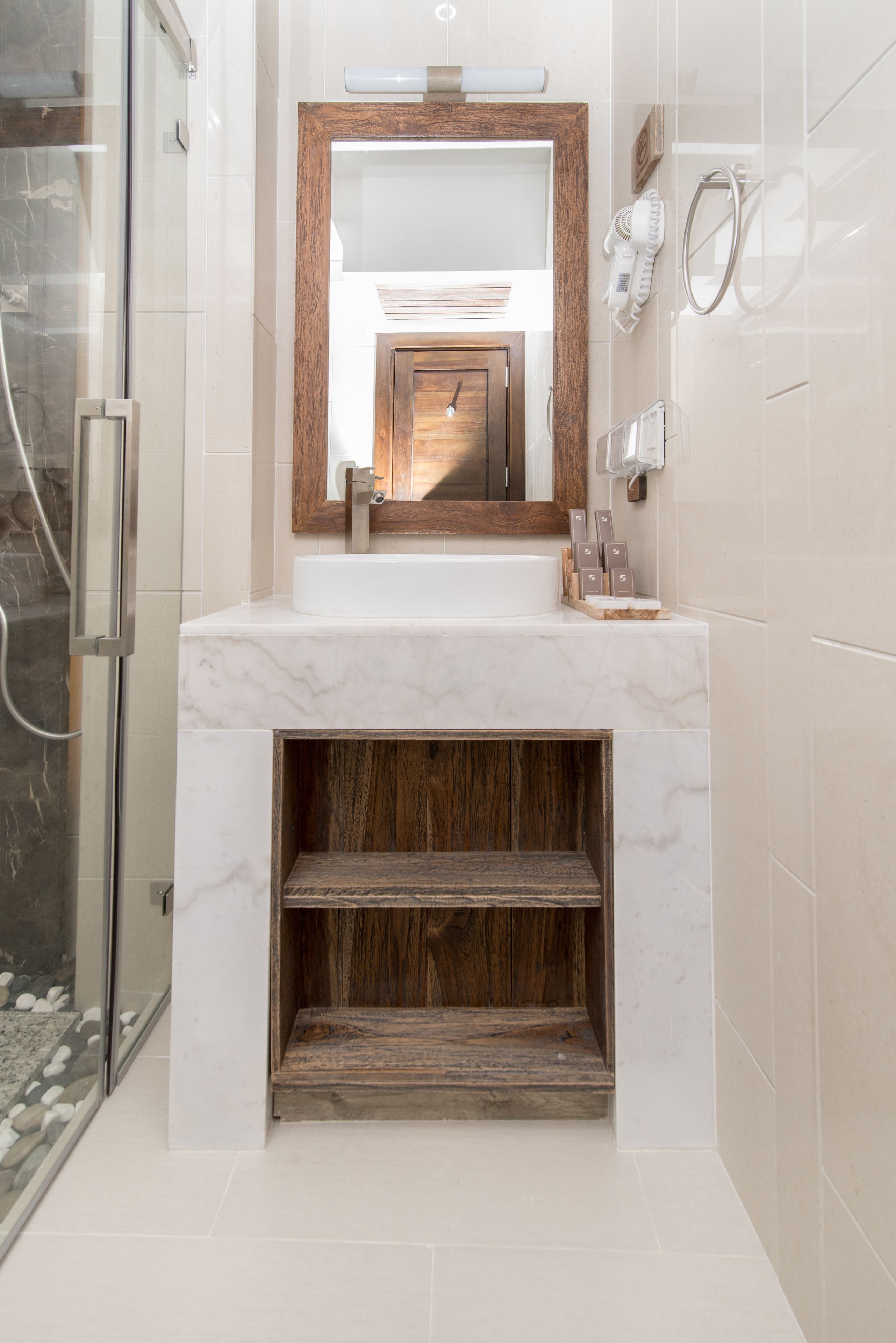 A bathroom with a marble sink, wooden vanity, and a glass shower enclosure.